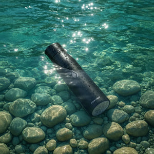 AQUA VAULT PureX Black water bottle on a bed of rocks and clear water