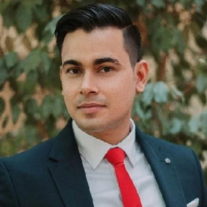 Founder, Owner & Managing Director of AQUA VAULT and SVK GROUP CO. wearing a dark suit with a red tie against a blurred green background