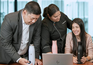 Three people with AQUA VAULT Self-Cleaning PureX Smart Water Bottles on a table in Corporate Set-up.