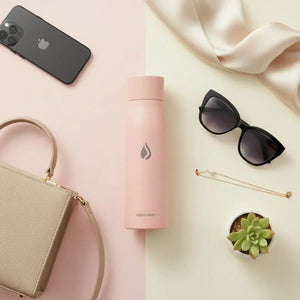 AQUA VAULT PureX pink bottle on pastel background with sunglasses, purse, iPhone, succulent, and jewelry.