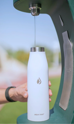 Aqua Vault White water bottle with silver cap being filled at a water dispenser, blurred background