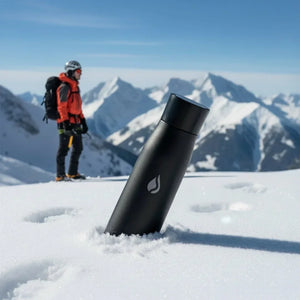 Black Colored AQUA VAULT PureX Self-Cleaning Premium Insulated Smart Water Bottle in the snow with a person in winter gear and mountains in the background.