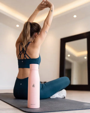 AQUA VAULT PureX UV-C self-cleaning smart water bottle with woman sits on a yoga mat in a bright room.