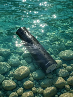 AQUA VAULT PureX Black water bottle on a bed of rocks and clear water